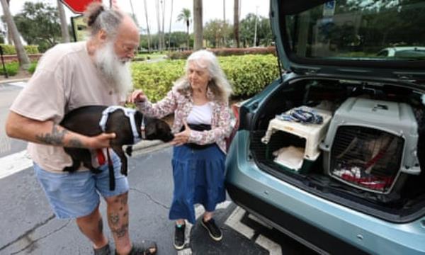 A man and woman holding their dog in front of open truck of a car
